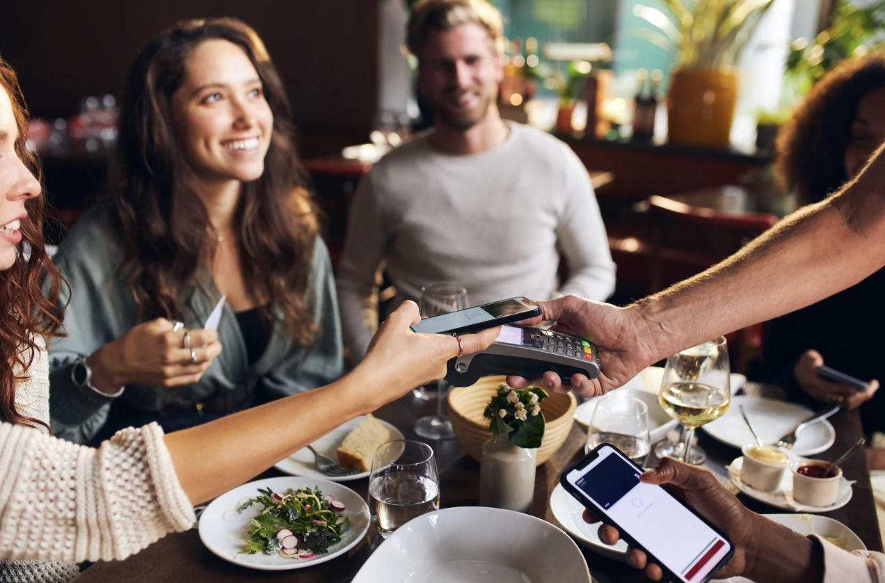 Restaurant guests using smartphone to tap-to-pay at card terminal
